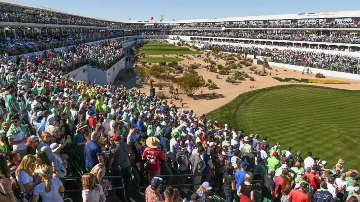 A lively scene from a professional golf tournament, with a crowd of spectators gathered around the course and grandstands in the background. The energy is palpable, with people cheering and enjoying the tournament experience.