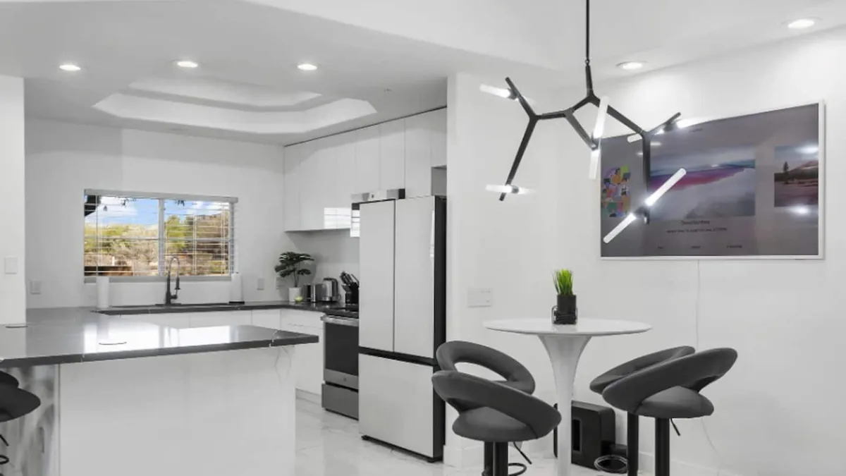 A vibrant kitchen scene with a central island, stylish modern lighting, a large smart TV, and bar stools for casual dining. The space exudes energy and sociability, ideal for hosting friends or enjoying family dinners in comfort.