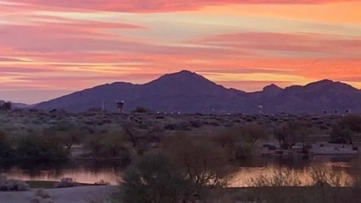 A serene sunset over distant mountains with a colorful sky reflected in a calm water surface. This tranquil view evokes the beauty of Scottsdale's natural surroundings and the peaceful moments available just beyond the apartment's doorstep.