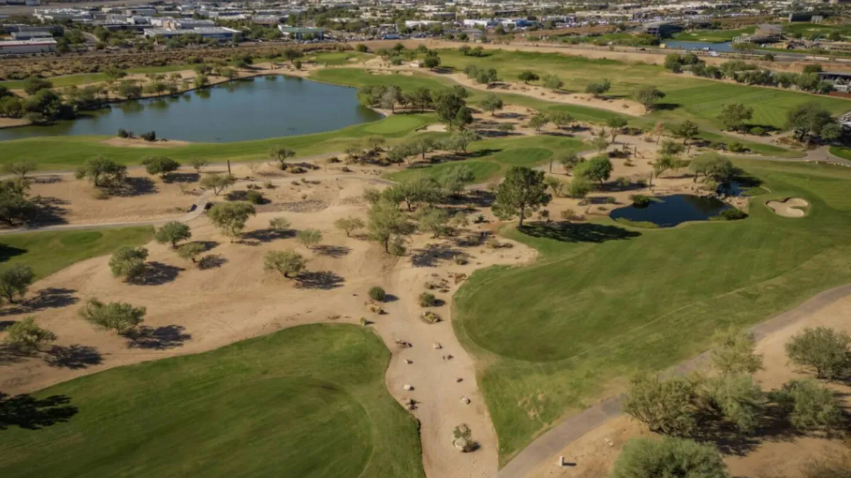 A sweeping view of a lush golf course featuring shimmering water features, manicured green lawns, and mature trees. The tranquil atmosphere is heightened by the reflection of sunlight on the water, suggesting a mild and inviting winter climate perfect for outdoor activities.