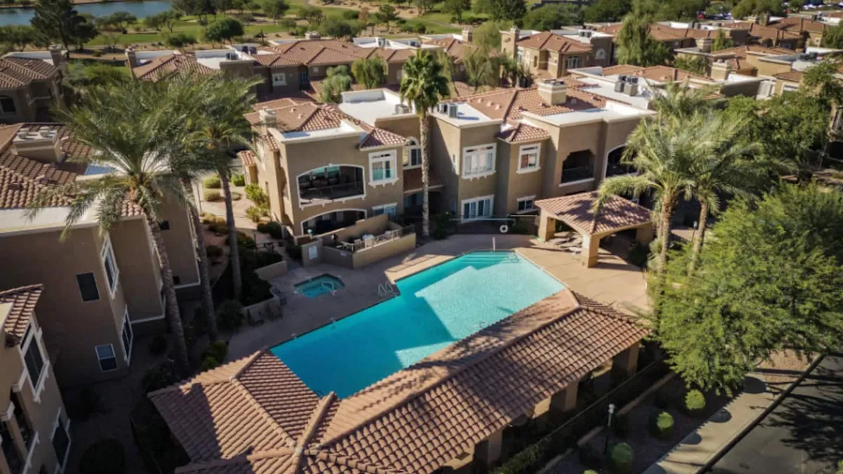 A vibrant community pool framed by palm trees, balconies, and landscaped gardens. The setting is bright and leisurely, inviting residents to relax, socialize, or unwind after a productive day.