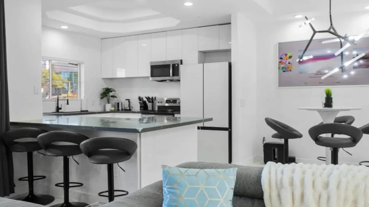 A cozy, welcoming kitchen with a spacious island, inviting bar stools, modern lighting, and decorative artwork. The area is clearly designed for both preparing and enjoying meals together, with a balance between function and style.