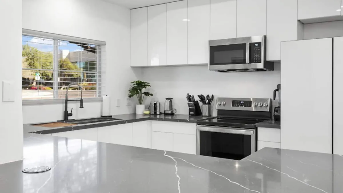 A bright, contemporary kitchen featuring a spacious island, sleek stainless steel appliances, and a window offering natural light. The design is open and inviting, perfect for meal prep or entertaining guests, and showcases ample countertops and modern amenities.